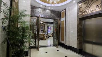 Un vestíbulo de hotel con una recepción, una planta en maceta, un ascensor y una pared decorativa.