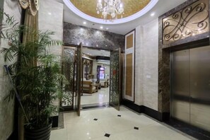 A hotel lobby with a reception desk, a potted plant, an elevator, and a decorative wall. - Fenghuang Huating Hostel (Guangze)