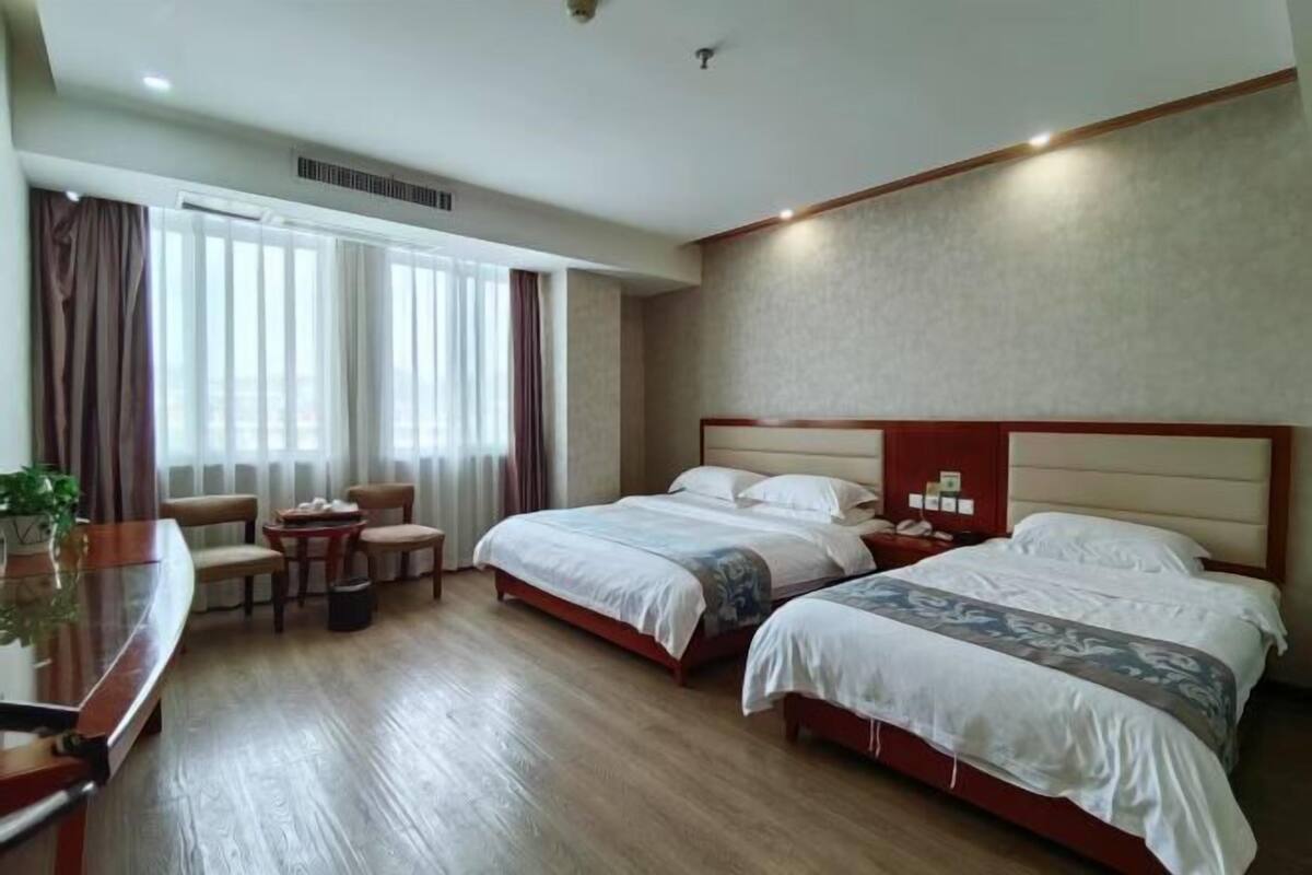A hotel room with two beds, a desk, a chair, a small table, and a window with curtains.
