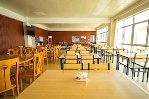 Un espace repas avec des tables et des chaises en bois, un tĂ©lĂ©viseur et de grandes fenĂȘtres.