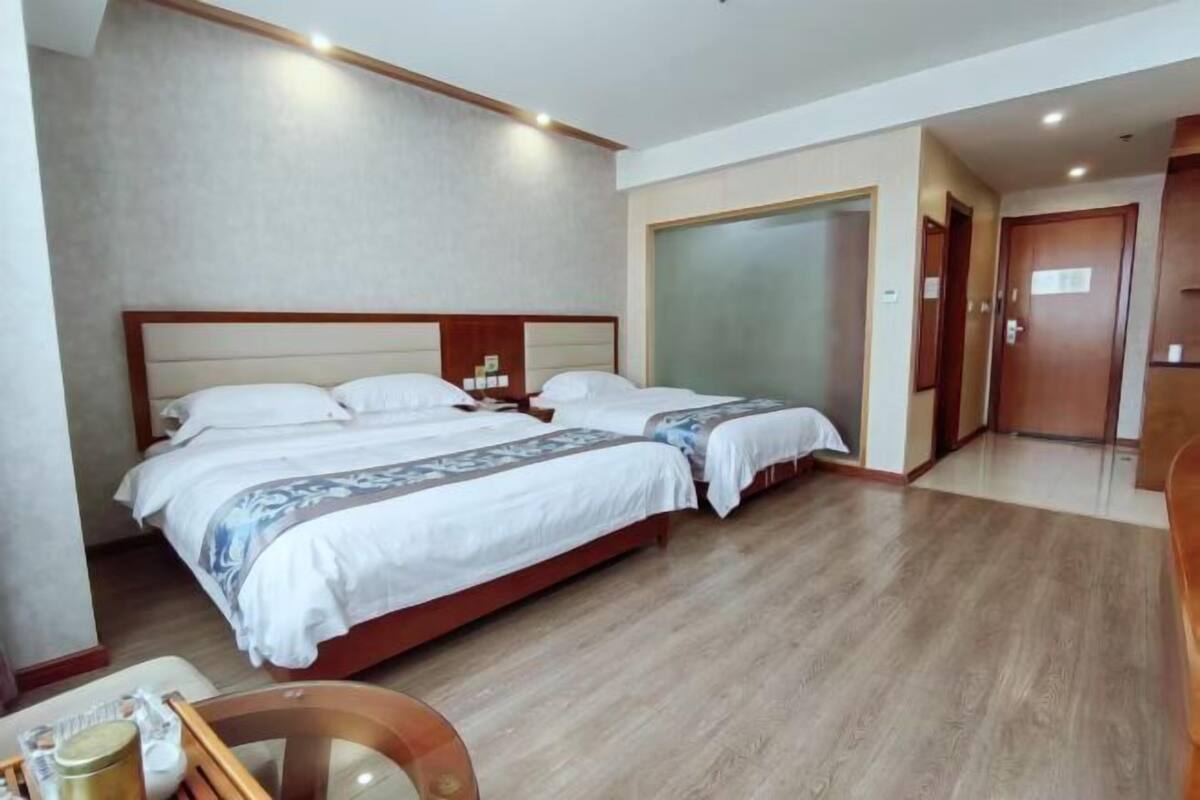 A hotel room with two beds, a wooden floor, a large mirror, and a wardrobe.