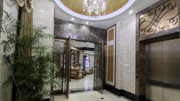 Un hall d’hôtel avec un sol en marbre, une plante en pot, un lustre et un ascenseur.