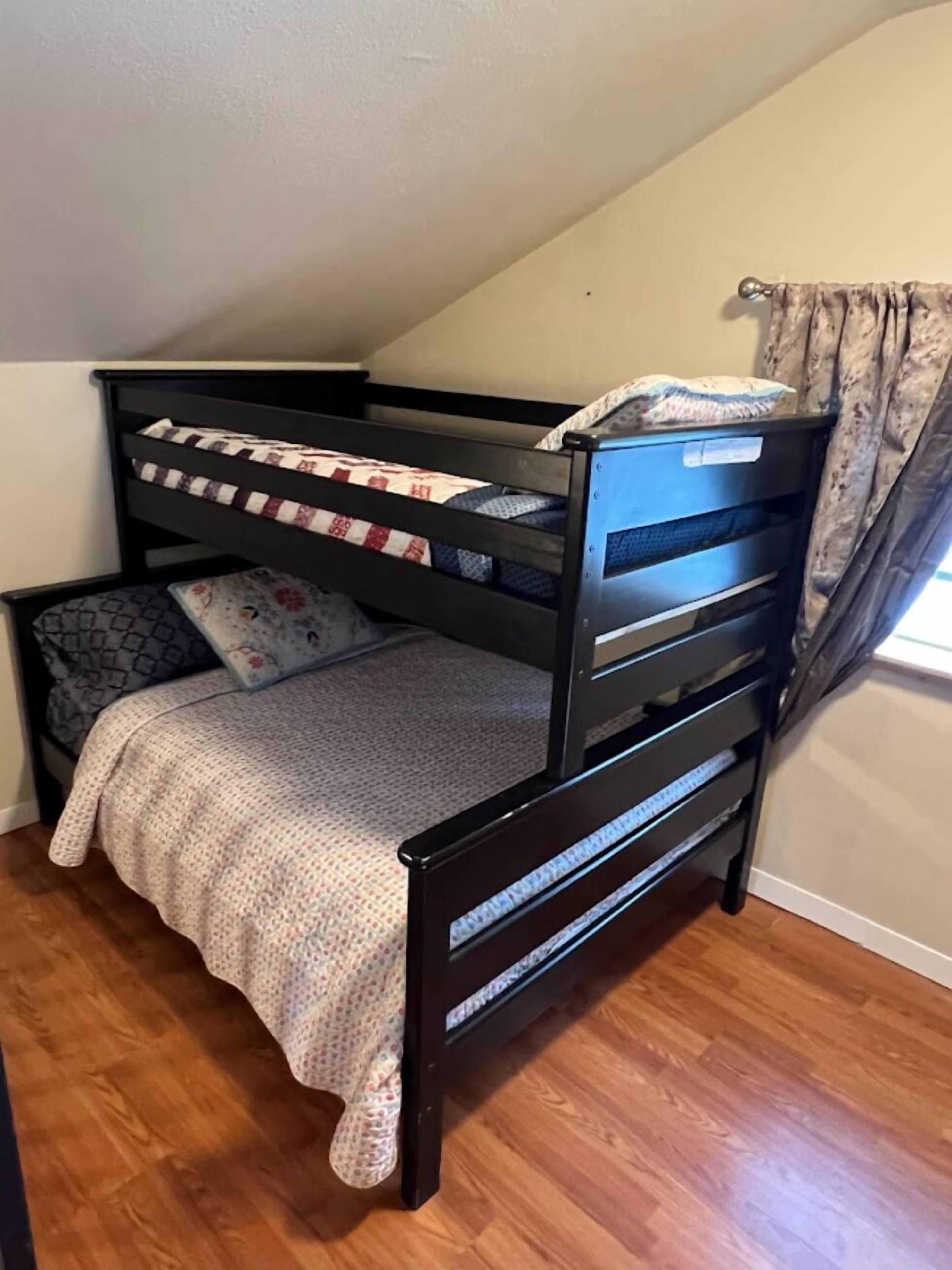 A bunk bed with a patterned bedspread and pillows, a small dresser, and a window with curtains.