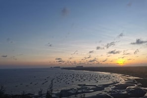 A coastal landscape with a beach and ocean during sunset. - Oceanside Hotel (Maoming)