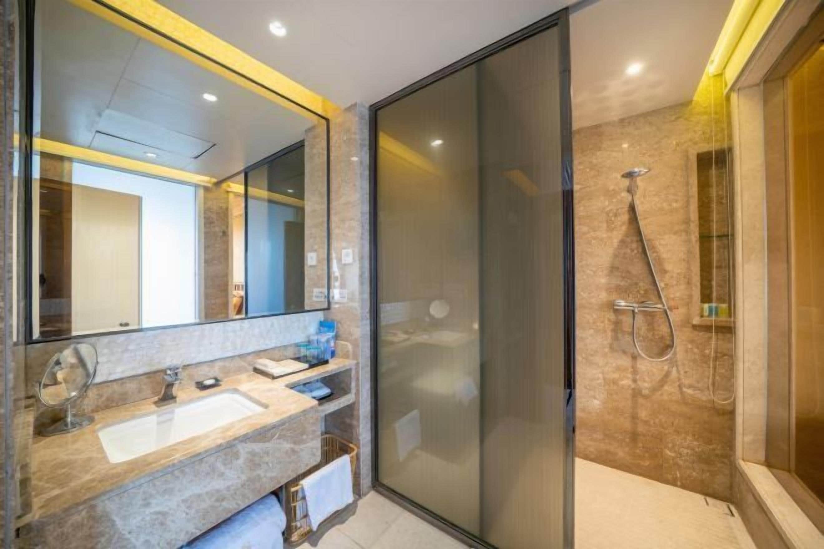 Un bagno moderno con cabina doccia in vetro, uno specchio grande e un piano lavabo in marmo.