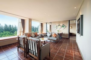 A spacious living area with a sofa set, a dining table, and a TV mounted on the wall.