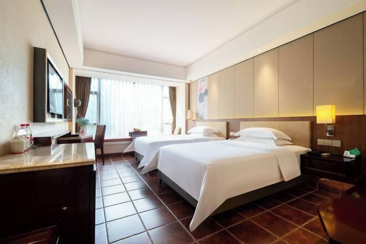 Hotellihuone, jossa on kaksi sänkyä, työpöytä, tuoli ja ikkuna, jossa on verhot.