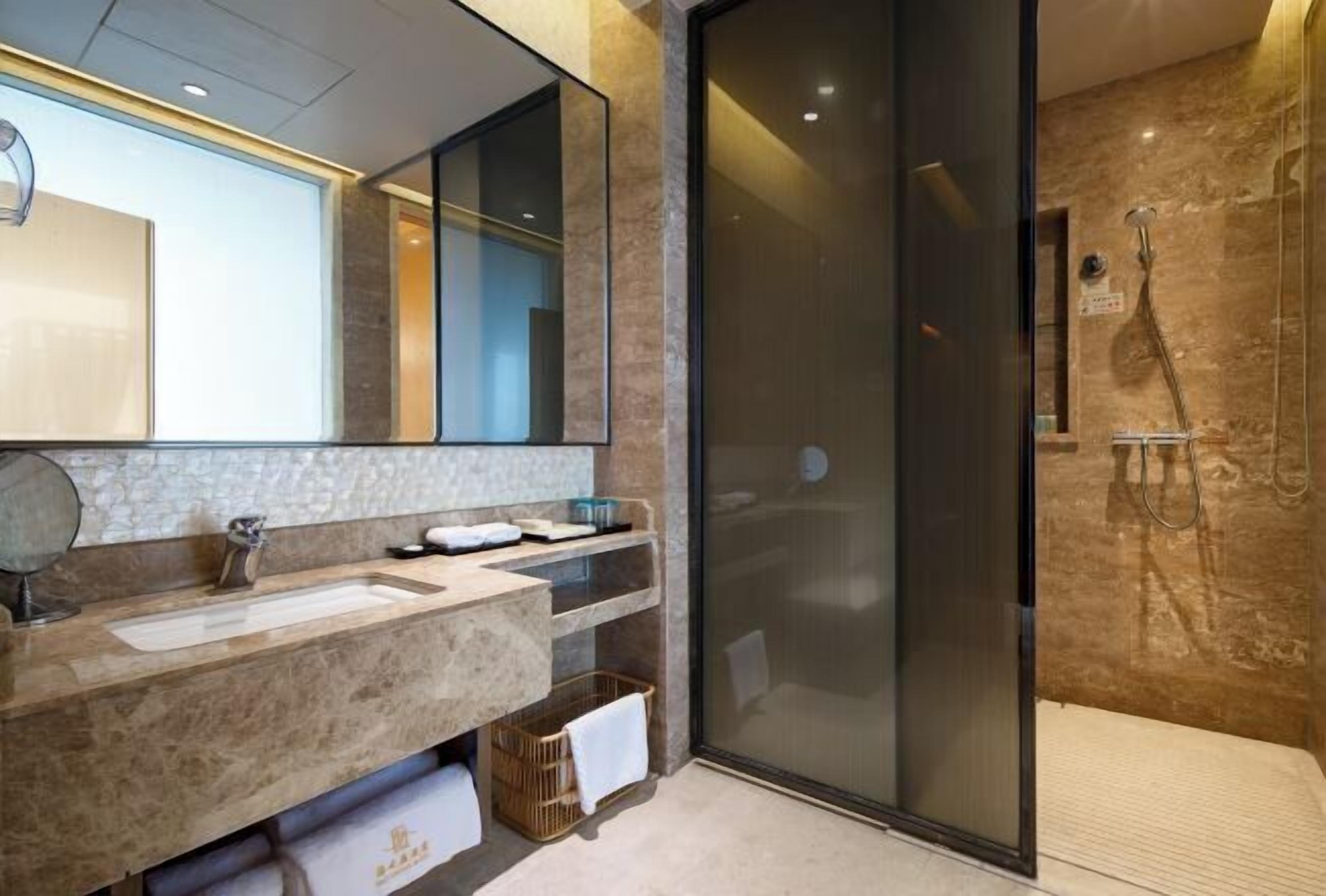 Un baño moderno con un espejo grande, dos lavamanos, una ducha y zona de ducha con paredes de vidrio.
