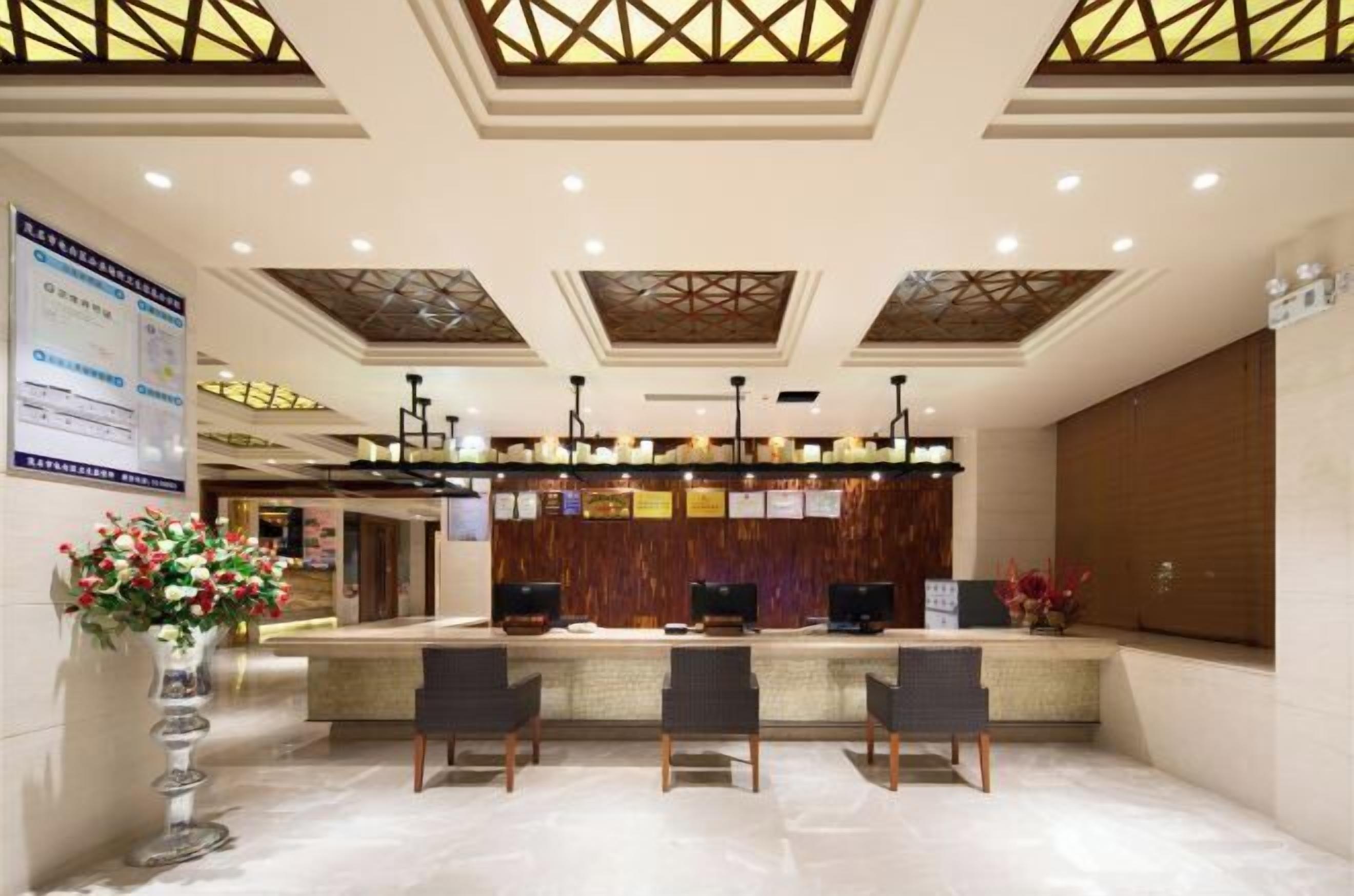 Ein Hotel-Empfangsbereich mit modernem Design, der einen Empfangstresen, eine Sitzecke und eine dekorative Vase mit Blumen zeigt.