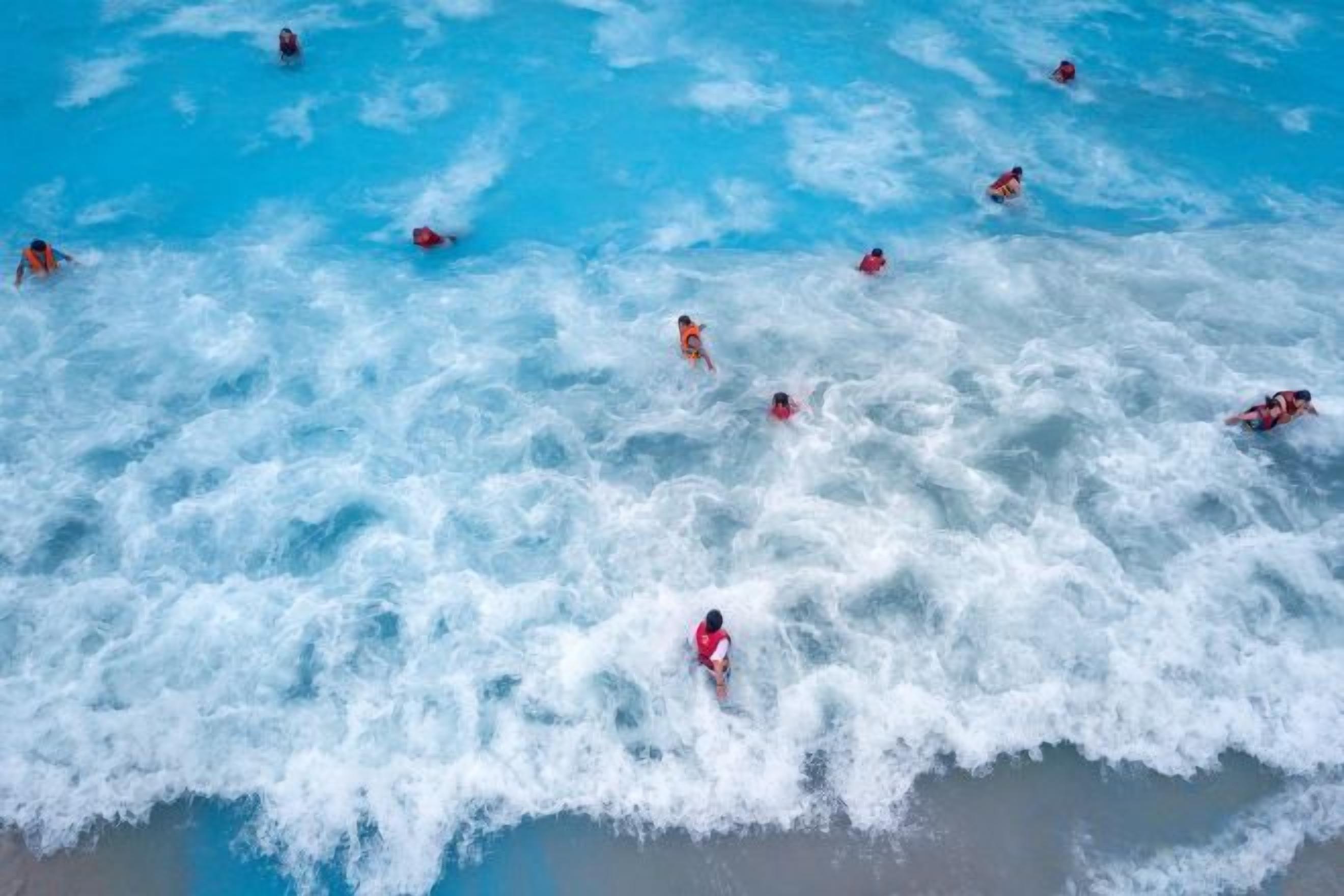 Une plage où l’on voit des gens nager et faire de la planche à voile.