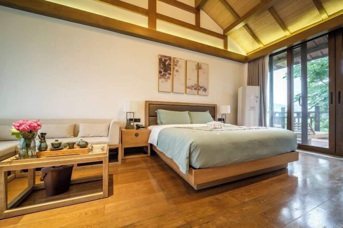 Un dormitorio con cama, mesitas de noche, una mesita auxiliar de madera y vistas a través de ventanas amplias.
