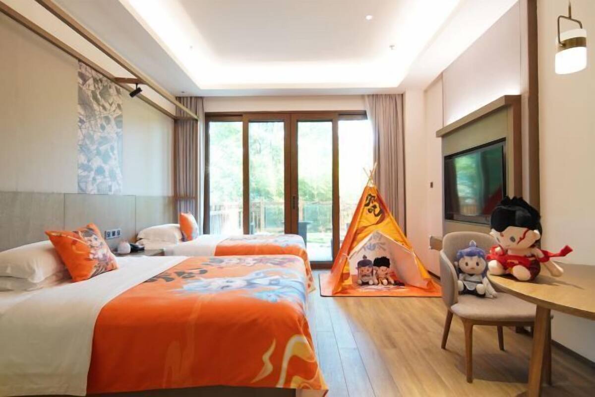 Habitación de hotel con dos camas, una tienda de campaña, peluches, un televisor y un ventanal grande.