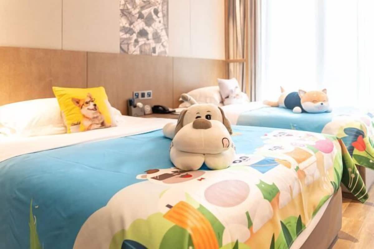 Habitación de hotel con dos camas, cada una con una colcha azul y un peluche sobre la cama.