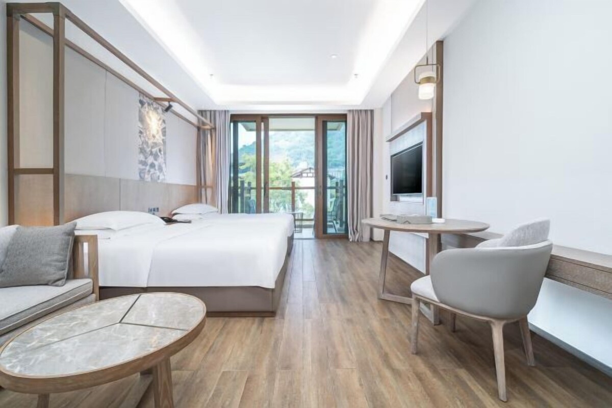 A hotel room with a bed, a sofa, a small table, a chair, and a TV.