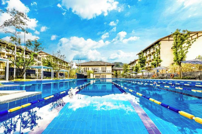 Une piscine à l’eau d’un bleu limpide, entourée d’immeubles et d’arbres.