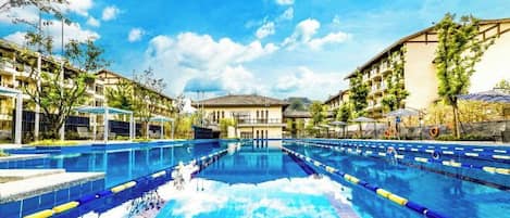 A swimming pool with clear blue water, surrounded by buildings and trees.