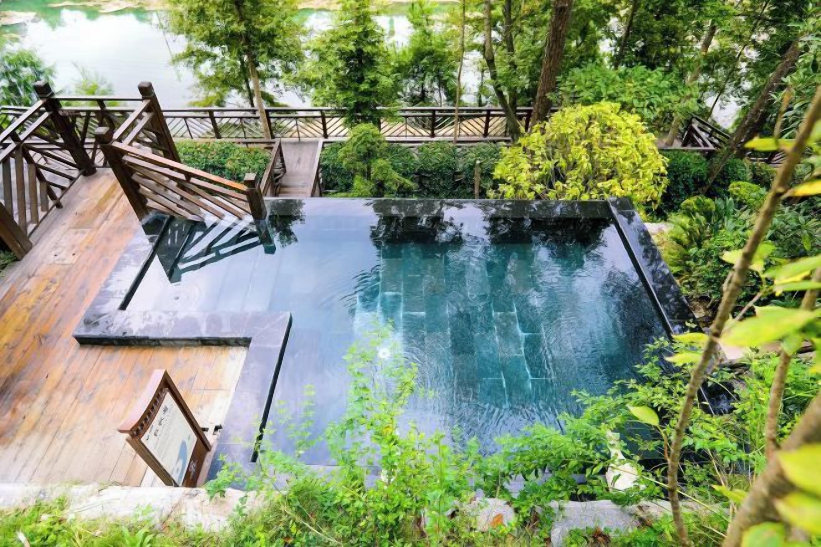 A rectangular pool with a wooden deck and a wooden railing.