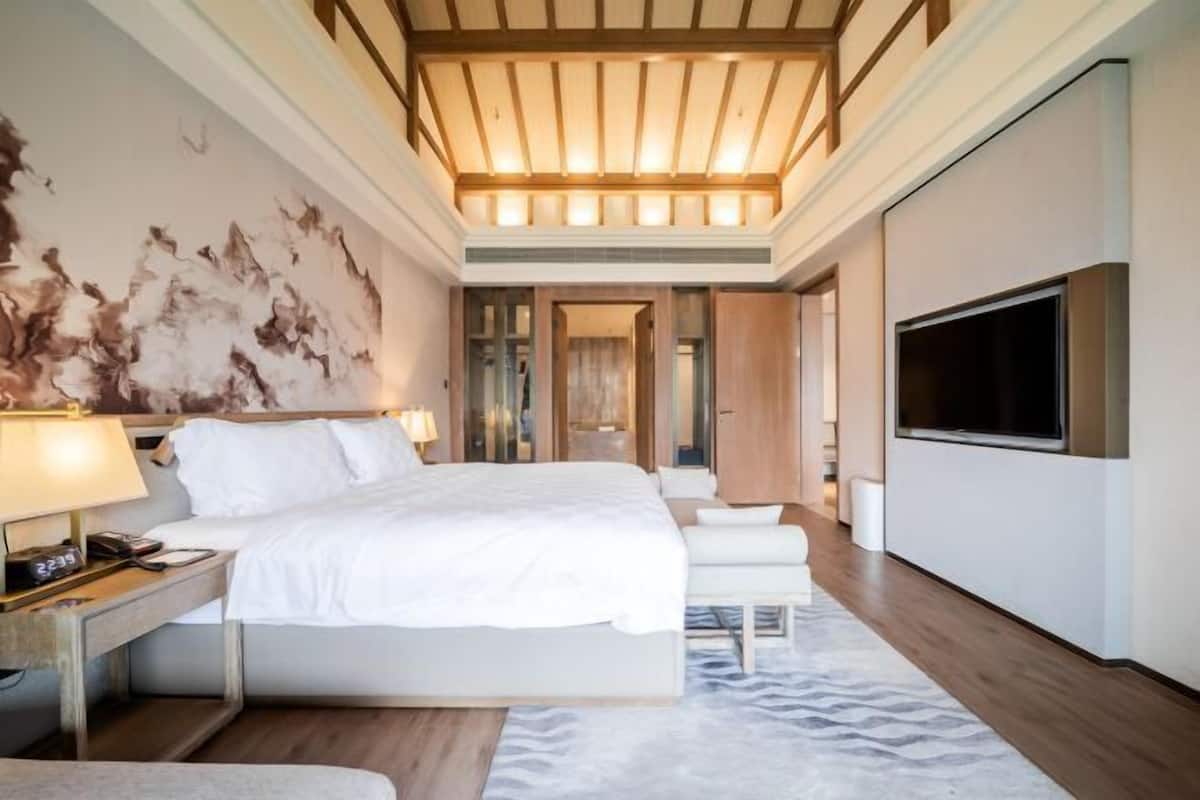 Una habitación de hotel moderna con una cama grande, mesitas de noche, un televisor de pantalla plana y un techo con vigas de madera.