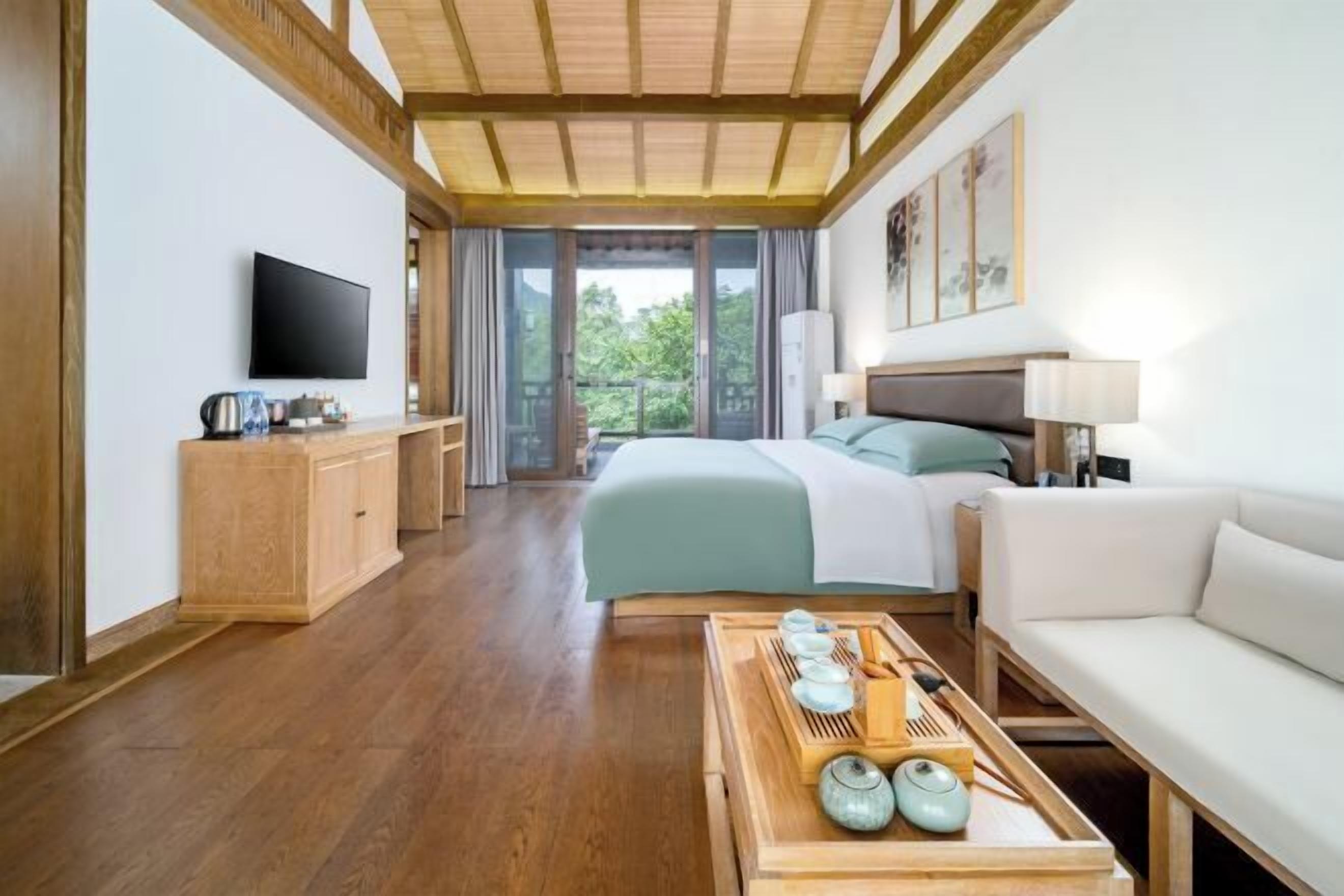 Habitación de hotel con cama, televisor, mueble de madera, sofá y bandeja con utensilios de cocina.