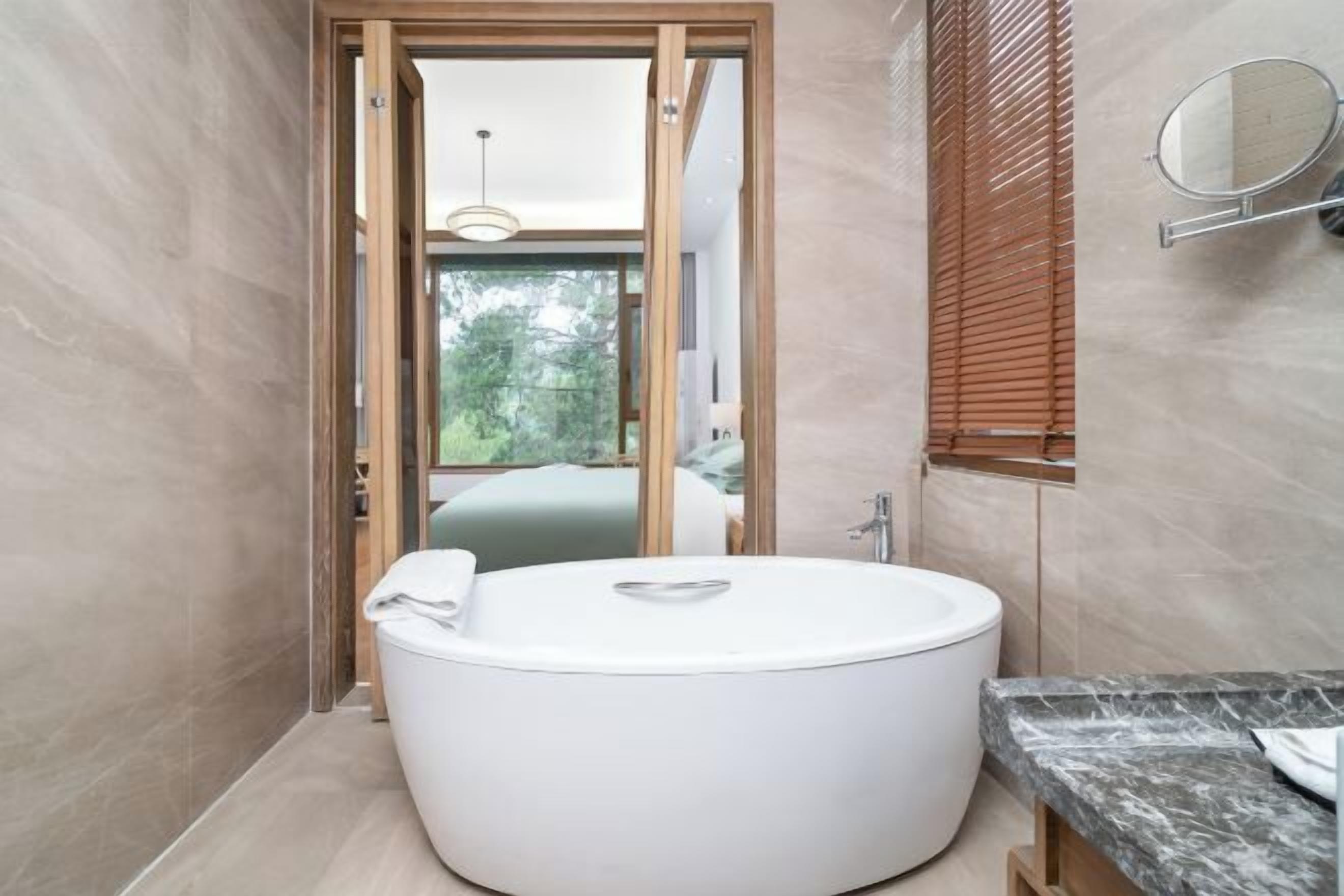 Un baño moderno con una bañera independiente, una encimera de mármol y vistas a un dormitorio a través de una puerta abierta.