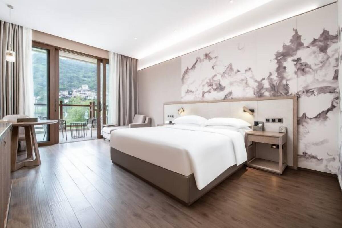 Una habitación de hotel moderna con una cama grande, un escritorio y vistas al exterior.