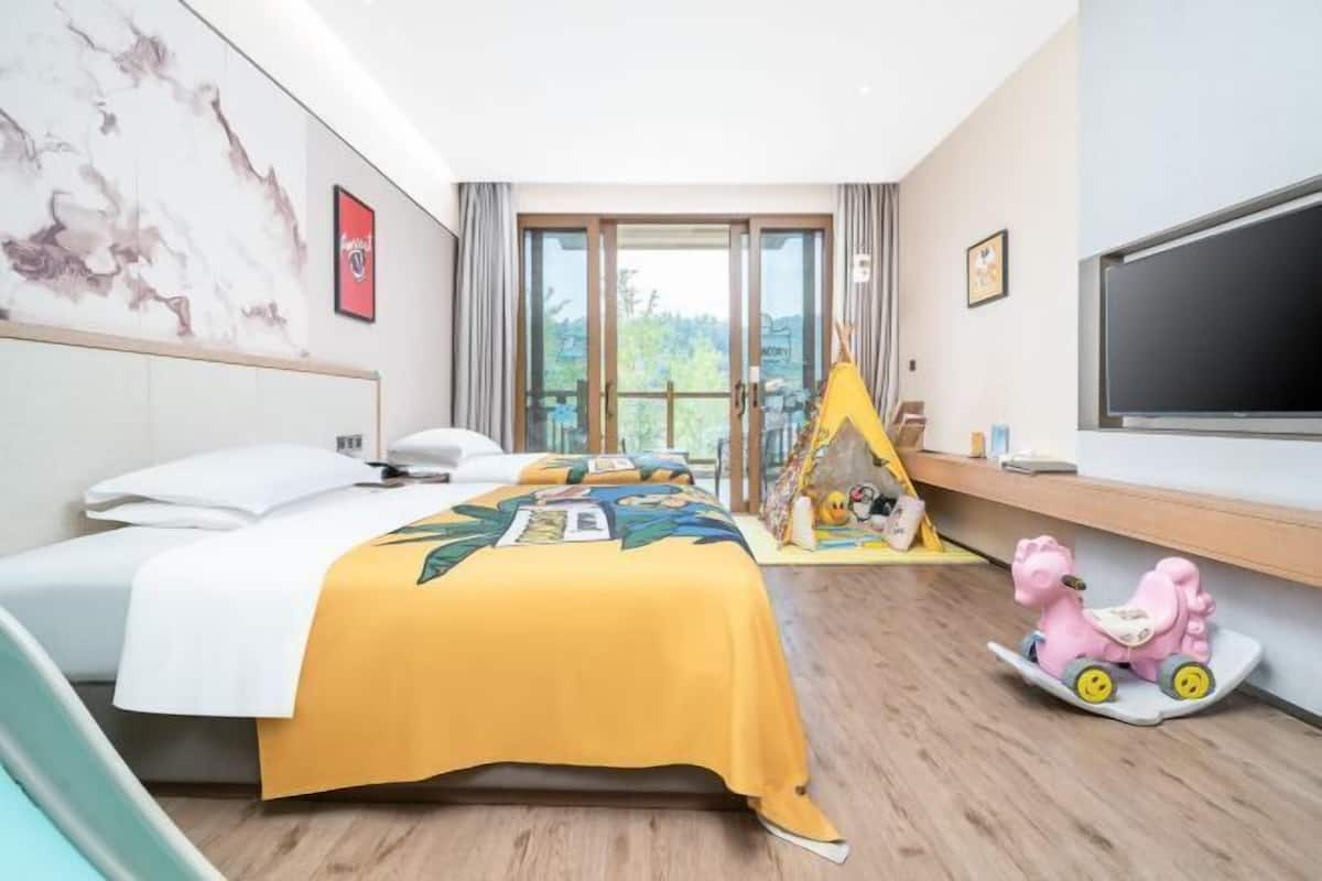 Habitación de hotel con cama, televisión, ventana con vistas y un pequeño rincón de juegos con un caballo de juguete.