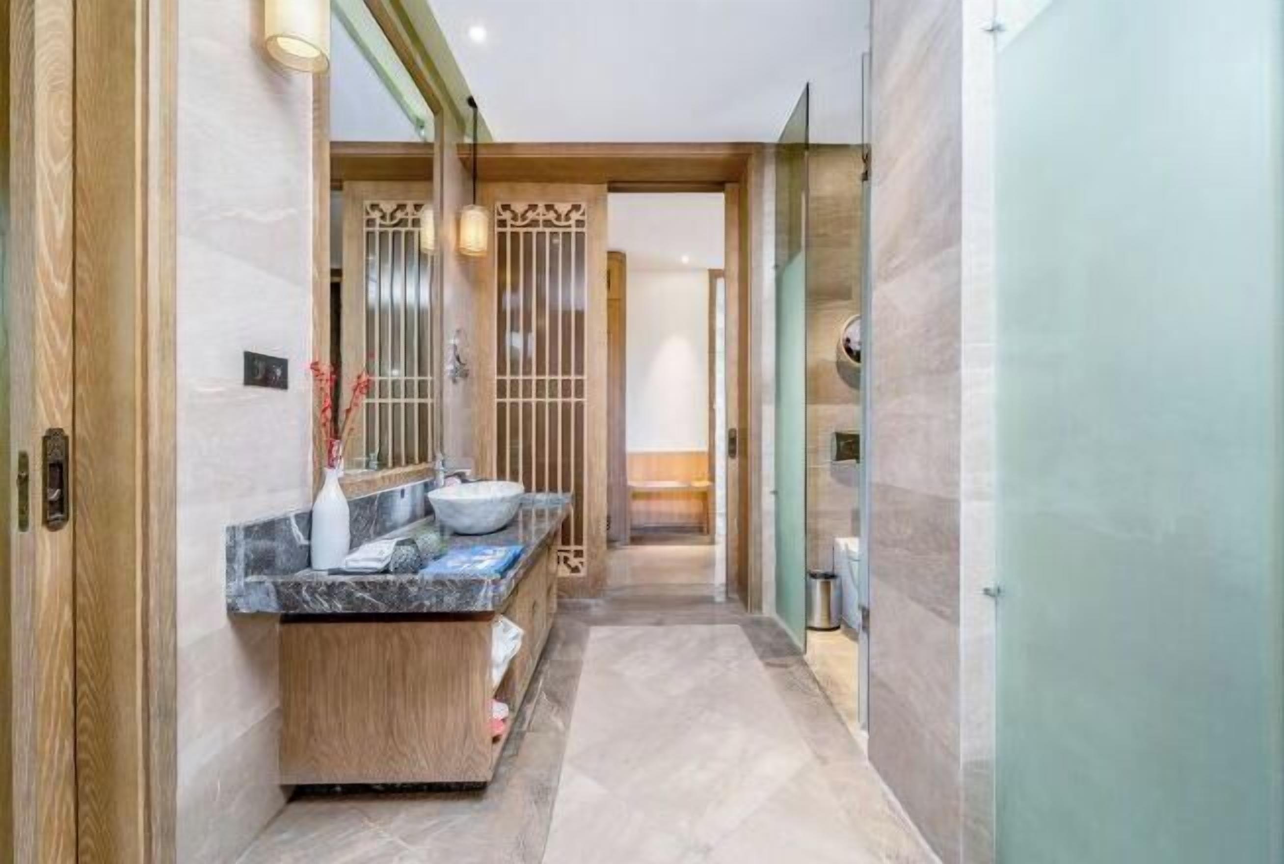 A modern bathroom with a marble sink, wooden vanity, and a glass shower enclosure.