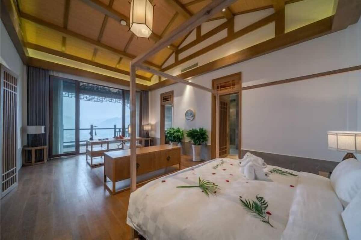 Habitación de hotel con cama, escritorio, silla, planta en maceta y vistas al exterior.