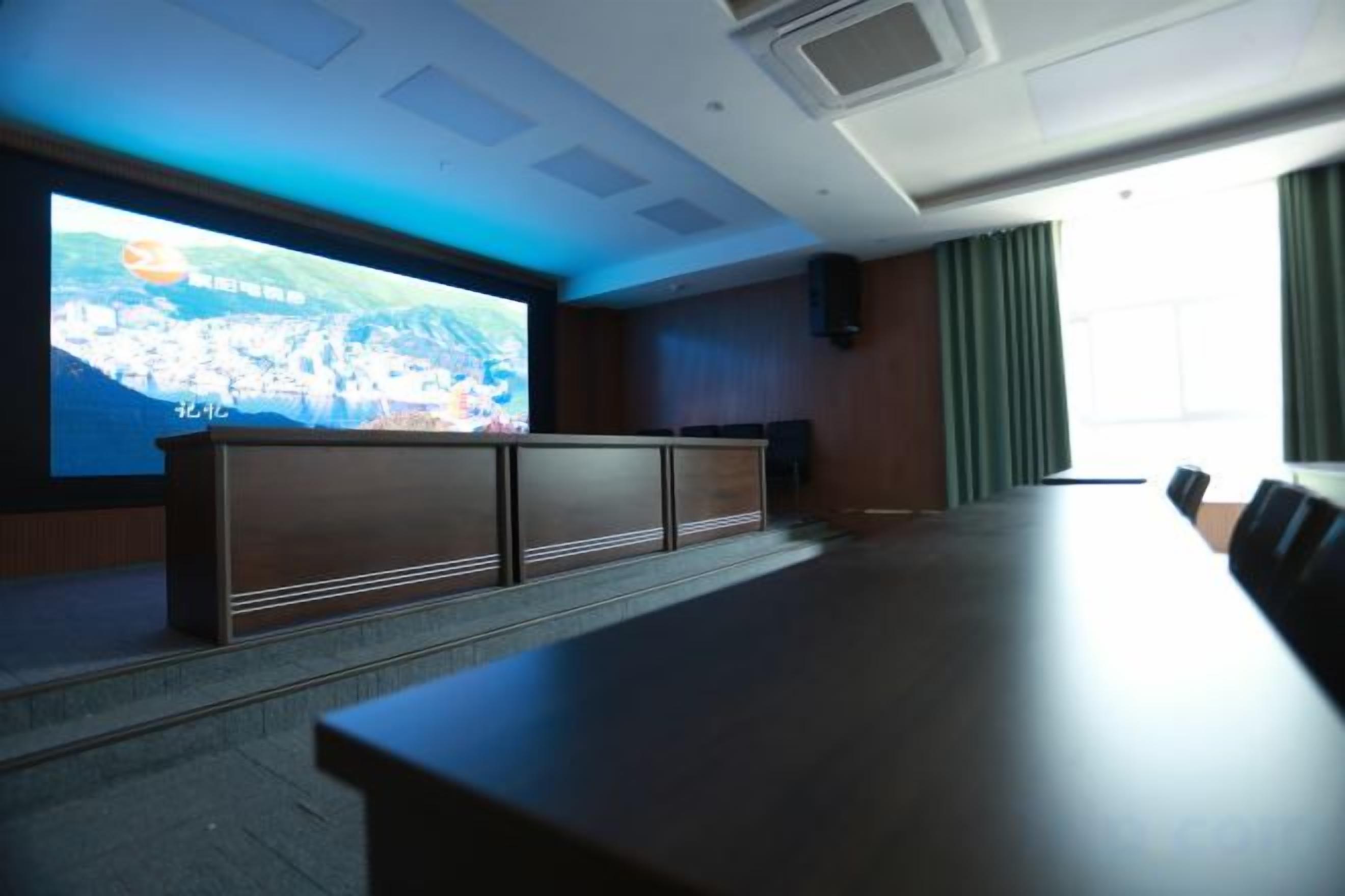 Une salle de conférence équipée d’un grand écran, d’une longue table et d’un espace pour s’asseoir.
