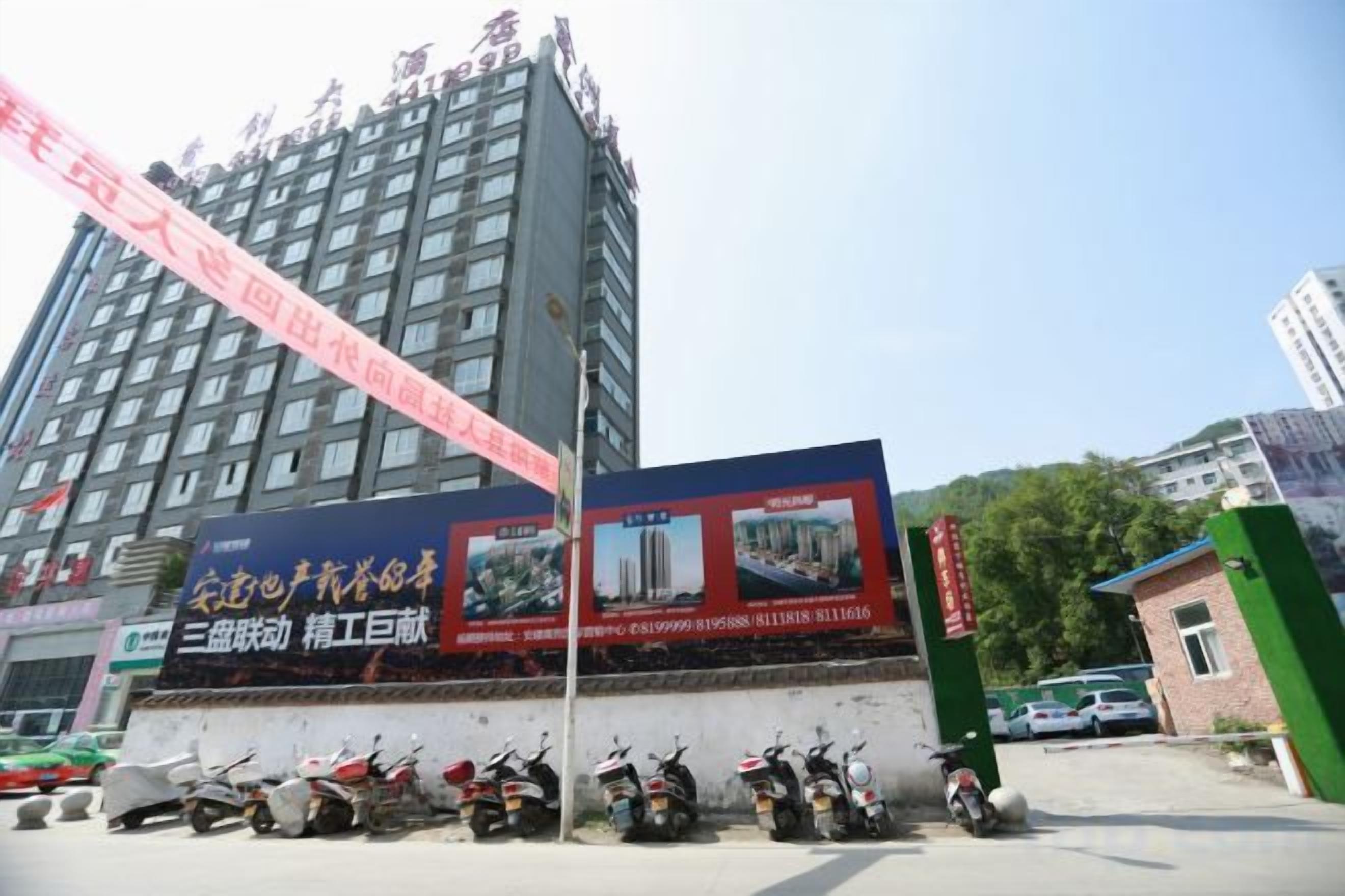 A multi-story building with a large billboard, parked scooters, and a green gate.