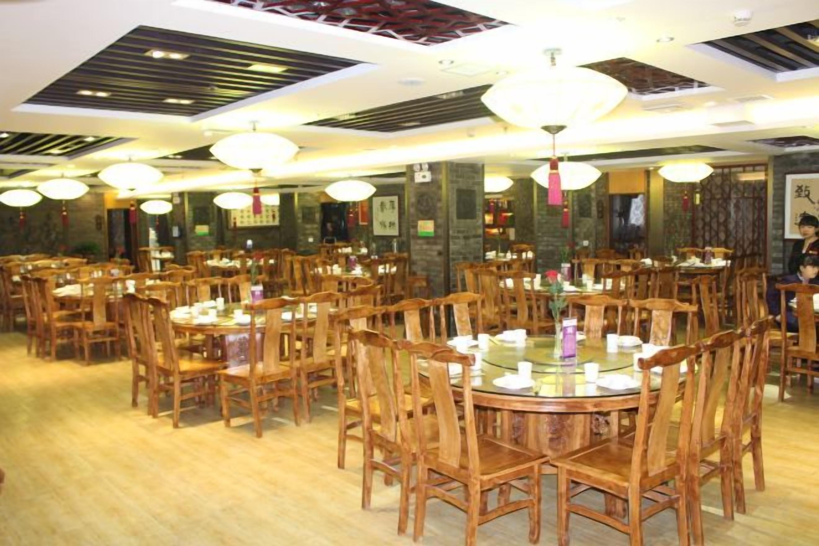 Un restaurante con varias mesas y sillas redondas, piso de madera y decoración china tradicional.