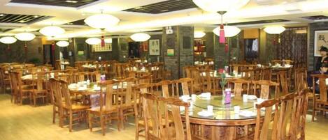 Un restaurante con varias mesas y sillas redondas, piso de madera y decoración china tradicional.