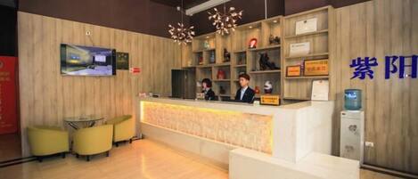 A reception area with a wooden reception desk, two receptionists, a television mounted on the wall, and a water dispenser.