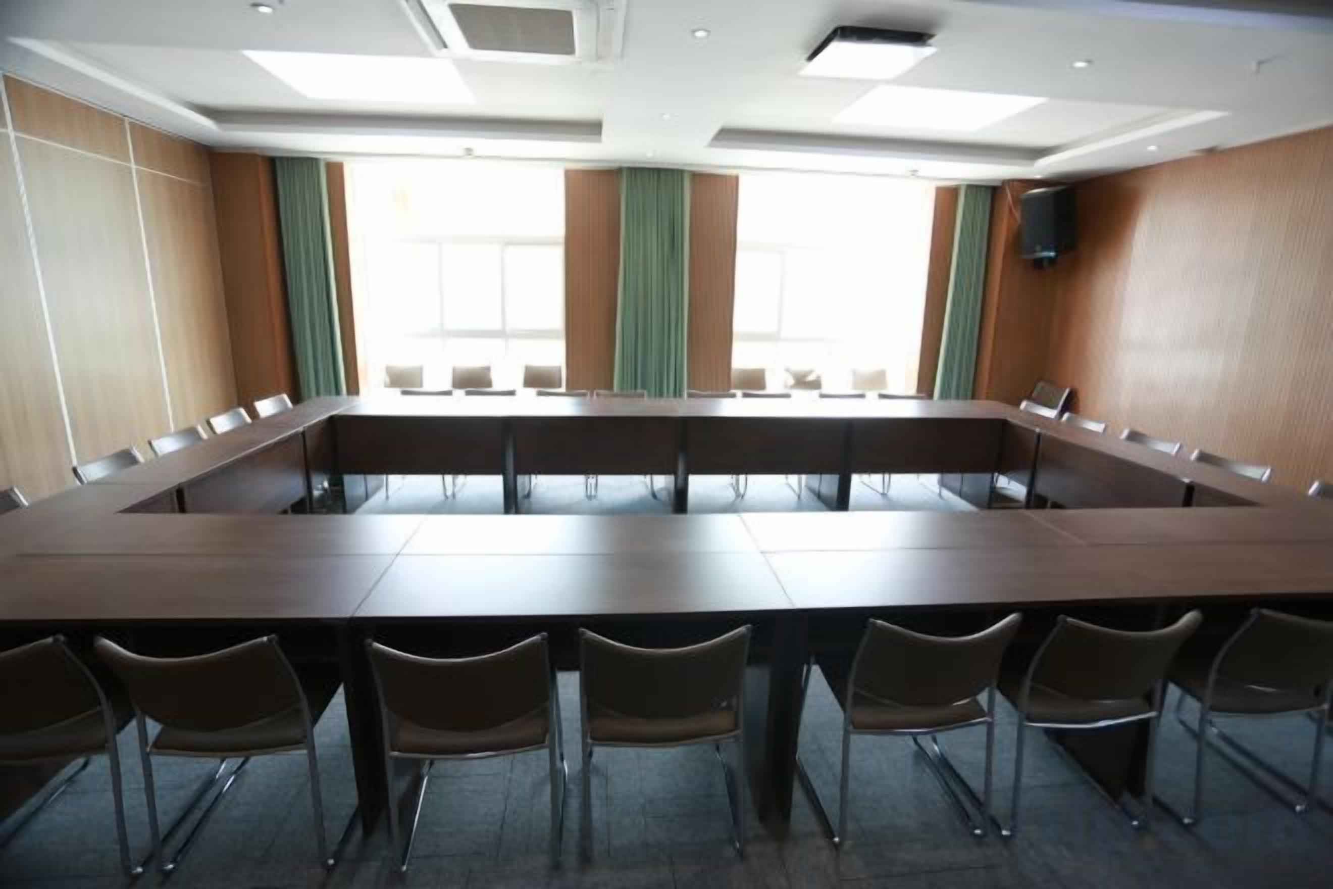 Un salón de conferencias con una larga mesa y sillas, ventanas amplias y un altavoz en la pared.