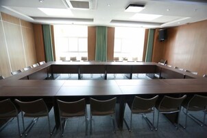 Un salón de conferencias con una larga mesa y sillas, ventanas amplias y un altavoz en la pared.
