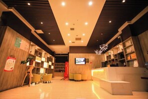 A hotel reception area with a modern design, featuring a reception desk, seating area, and a television screen.