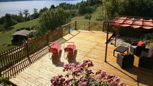 A wooden deck with outdoor seating, a view of a lake, and surrounding greenery. - Superior apartment with 2 balconies with lake and mountain view (Starfach)