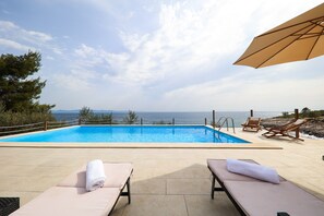 Une piscine avec vue sur la mer, des chaises longues et un parasol.