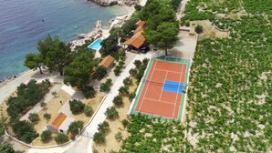 Vista aérea de una propiedad costera con cancha de tenis, piscina y viñedo.