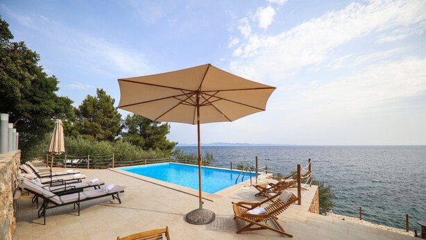 Un área junto a la piscina con sillas de descanso y una sombrilla, con vistas al mar.