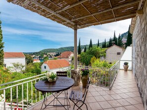 Ein überdachter Außenbereich mit Tisch und Stühlen, einem Blumentopf und Blick auf eine Stadt mit roten Dächern und Grünflächen.