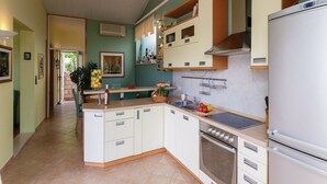 A kitchen with white cabinets, a built-in oven, and a refrigerator. There is a window with curtains and a door leading to another room.