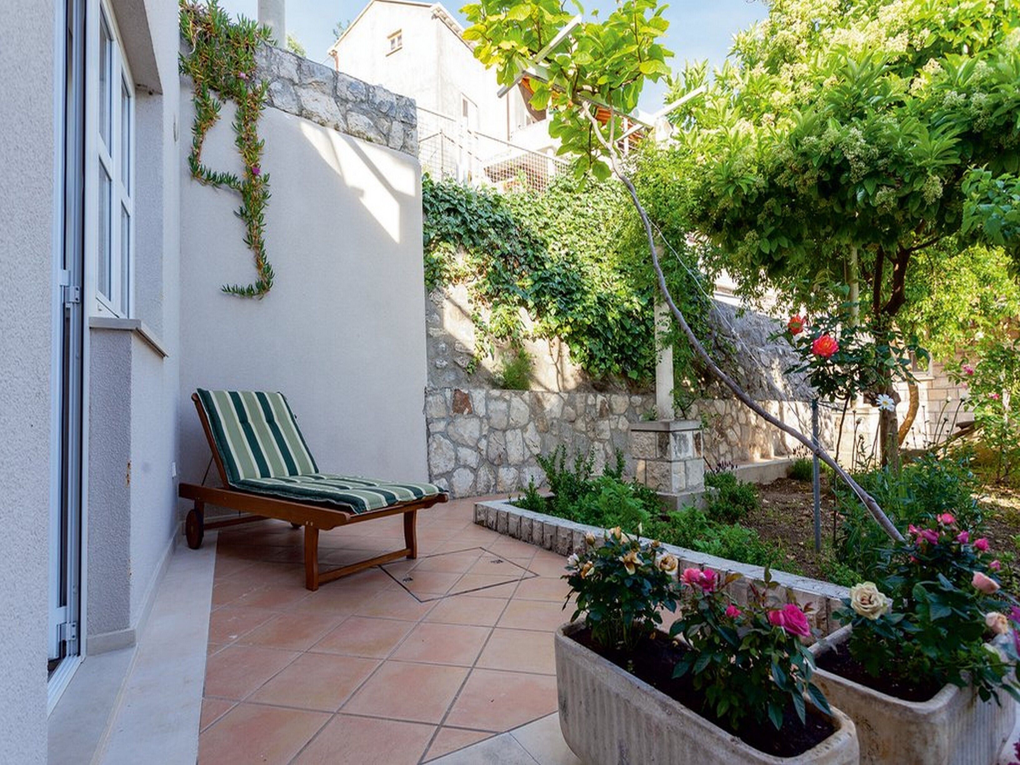 Un patio con una silla lounge a rayas, un muro de piedra y macetas con flores.
