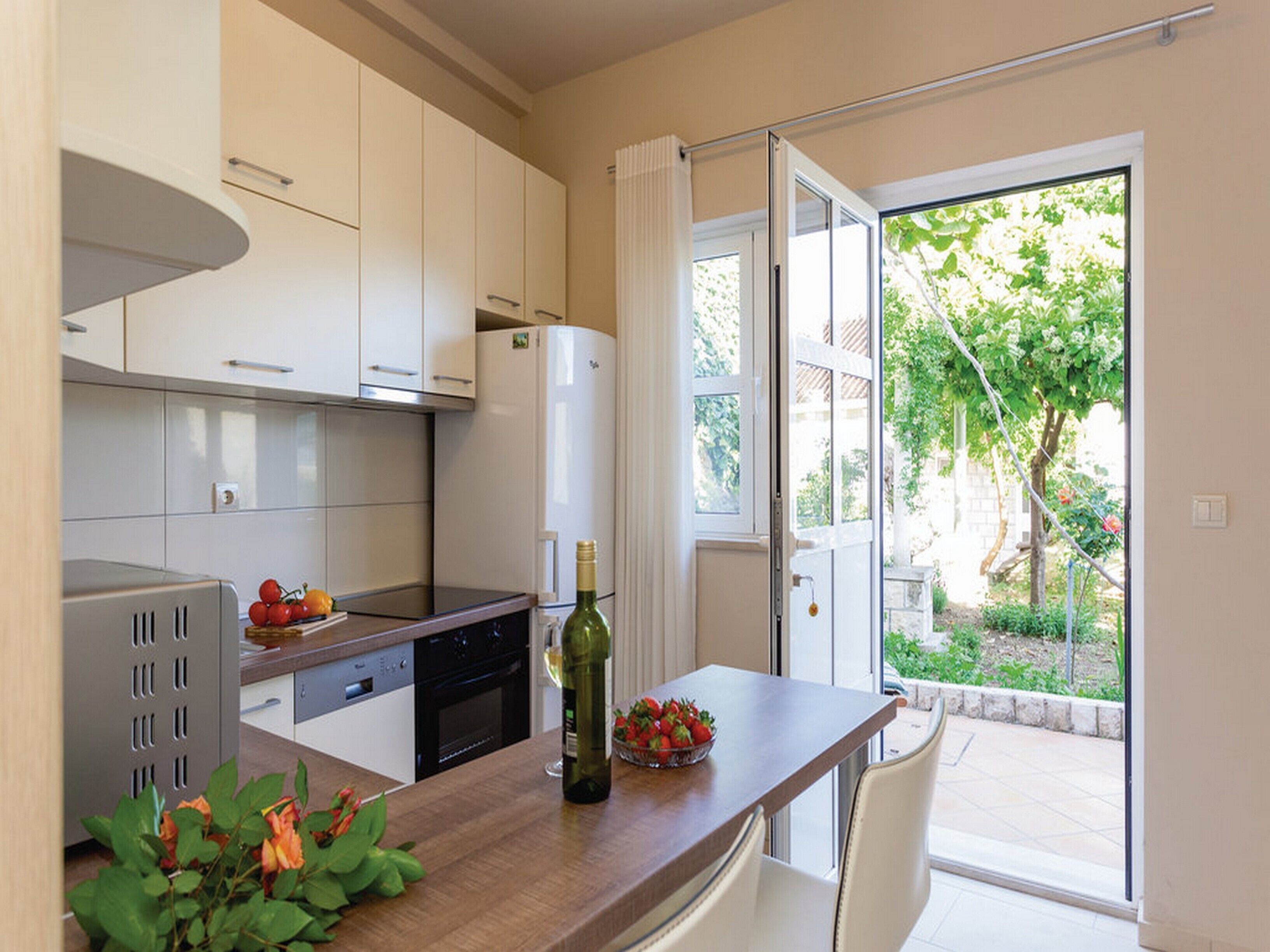 A modern kitchen with white cabinets, a built-in oven, and a dining area with a table and chairs.