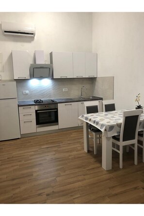 A compact kitchen with white cabinets, a built-in oven, and a dining area with a table and chairs.