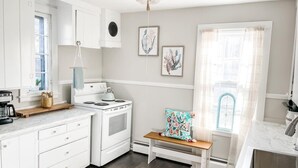 Una cocina moderna con muebles blancos, estufa, fregadero y un banco con cojín floral.
