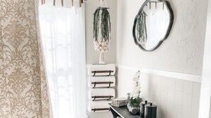 Un baño con cortina de ducha, una lámpara colgante de macramé, un espejo y un perchero para toallas.