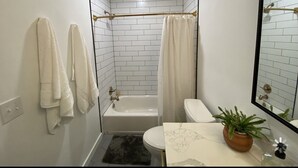 Un baño con una bañera blanca, un inodoro y un lavabo con una planta en maceta.