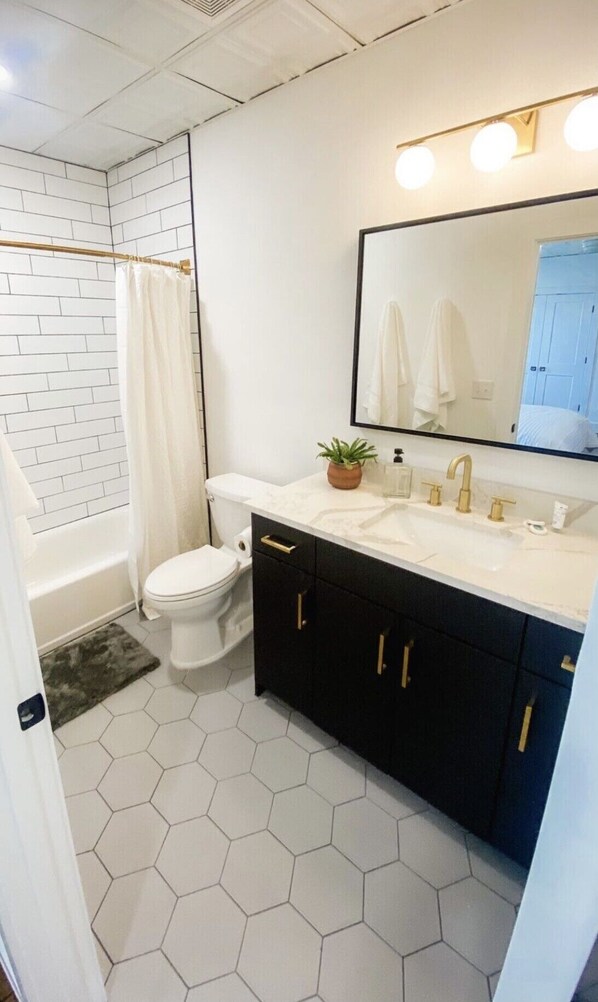 A bathroom with a white toilet, a bathtub with a white shower curtain, a sink with a mirror above it, and black cabinets.