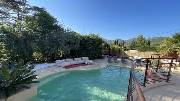 Ein Garten mit Schwimmbecken, einem beigen Sofa und einer Holzterrasse.